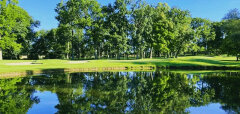 Jezero s odrazem stromů a zelené golfové hřiště za ním