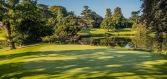 Golfové hřiště s jezírkem a mostkem v parku s domem v pozadí