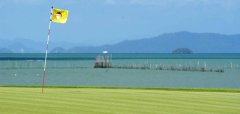 Golfové hřiště s vlajkou u moře a horami v pozadí