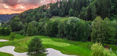 Golfové hřiště s pískovými bunkry a lesnatým pozadím při západu slunce