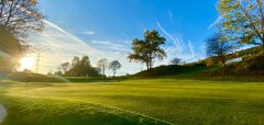 Golfové hřiště za slunečného dne s modrou oblohou a stromy