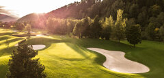 Golfové hřiště se zelení a pískovými bunkry u lesa při západu slunce