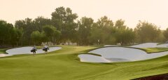 Golfové hřiště s hráči a pískovými bunkry za soumraku
