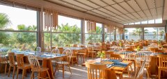 Interiér restaurace s dřevěným nábytkem a výhledem na palmy Lyttos Beach