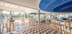 Interiér moderního baru s dřevěným nábytkem a výhledem na palmy Lyttos Beach