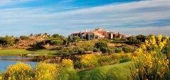 Golfové hřiště s jezírkem a budovou v pozadí za keři s žlutými květy