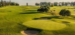 Golfové hřiště s greenem, bunkry a stromy za slunečného dne