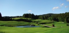 Golfové hřiště s jezírkem a lesy v pozadí