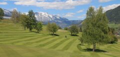 Golfové hřiště s kopci a zasněženými horami v pozadí