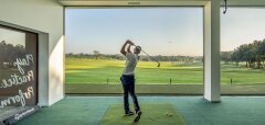 Muž hrající golf v interiéru s výhledem na golfové hřiště