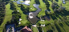 Zelené golfové hřiště s několika stromy a mlhou v pozadí