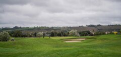 Golfové hřiště s hráči a pískovým bunkrem za šedé oblohy