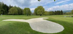 Golfové hřiště s pískovým bunkrem a stromy v pozadí