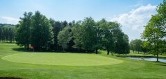 Golfové hřiště s jamkou, stromy a jezírkem za zelení