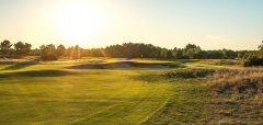 Golfové hřiště při západu slunce s pískovým bunkrem a vlajkou