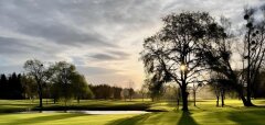 Golfové hřiště s jezírkem a stromy při západu slunce