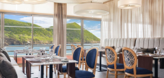 Interiér restaurace s výhledem na moře a zelené kopce