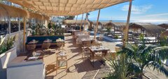 Venkovní restaurace s dřevěnými stoly a výhledem na pláž a moře