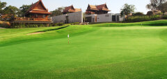 Golfové hřiště s vlajkou a tradiční thajské stavby v pozadí