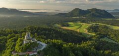 Zřícenina hradu na kopci obklopeném lesy a golfové hřiště v dálce
