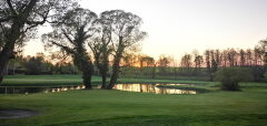 Golfové hřiště s jezírkem a stromy při západu slunce