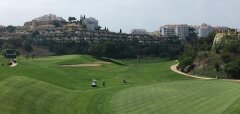Golfové hřiště s hráči a budovami na kopci v pozadí
