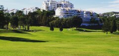 Zelené golfové hřiště s bílými budovami v pozadí