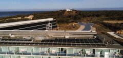 Moderní hotelová budova s terasami a solárními panely u lesa a moře