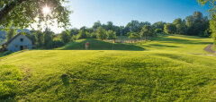 Golfové hřiště za slunečného dne s hráčem a domem v pozadí