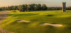 Golfové hřiště s pískovými bunkry a kamennou věží v pozadí