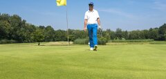Golfista na greenu s golfovým míčkem a žlutou vlajkou