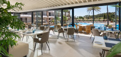 Interiér restaurace s výhledem na bazén a palmy v La Cala Hotelu