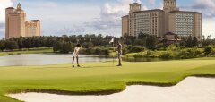 Dva lidé hrají golf na hřišti u jezera a hotelu Ritz-Carlton