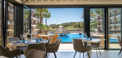 Interiér restaurace s výhledem na bazén a palmy v La Cala Hotelu