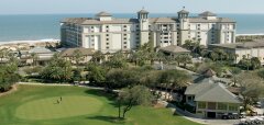 Golfové hřiště s resortem u oceánu a palmami v pozadí