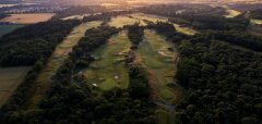 Letecký pohled na golfové hřiště obklopené lesy při západu slunce
