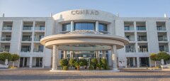Vstupní část hotelu Conrad s kulatou přístřeškovou střechou a keři.