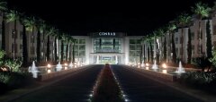 Noční pohled na osvětlený hotel Conrad s palmami a fontánami