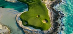 Pohled na golfové hřiště u oceánu s palmami a skalnatým pobřežím
