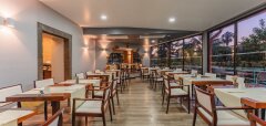 Interiér restaurace s dřevěnými stoly a židlemi u velkých oken