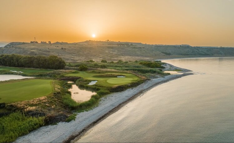 Golfové hřiště u moře s pískovým bunkrem a věží v pozadí