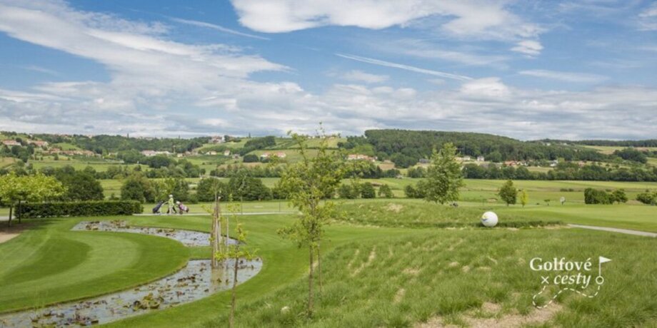 Golfové hřiště s jezírkem a kopcovitou krajinou v pozadí