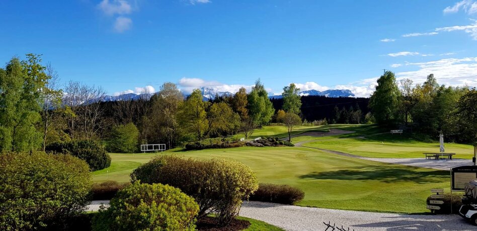 Golfové hřiště s trávníkem, stromy a horami v pozadí