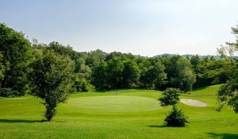 Golfové hřiště se zeleným greenem a stromy v pozadí