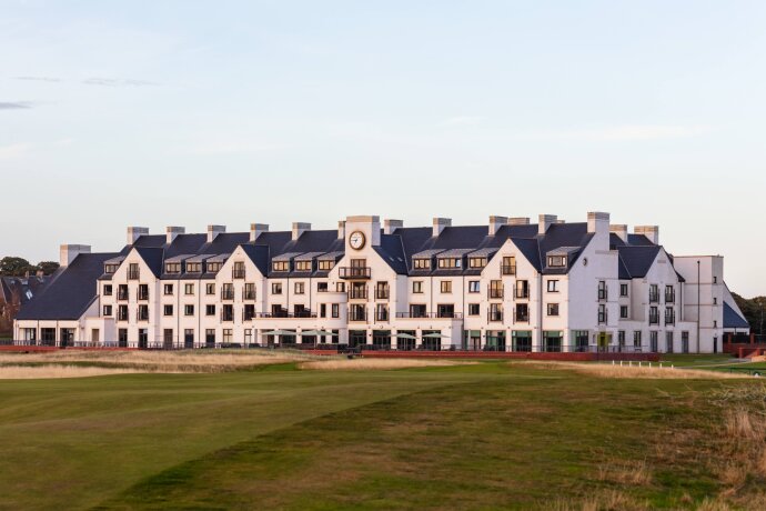 Bílá budova hotelu s hodinami uprostřed a zelený golfový trávník před ní