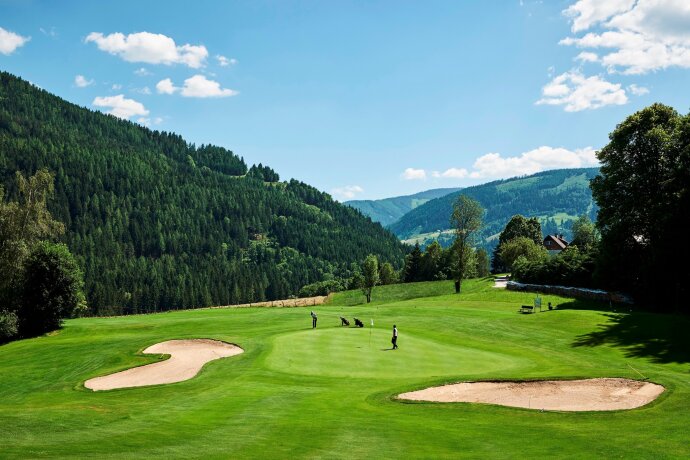 Golfové hřiště s hráči v horské krajině za slunečného dne